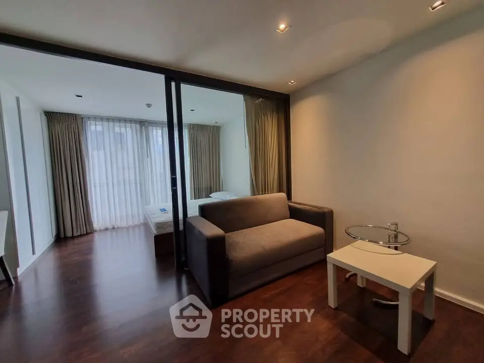 Modern living room with cozy sofa and glass table, adjacent to a bright bedroom.