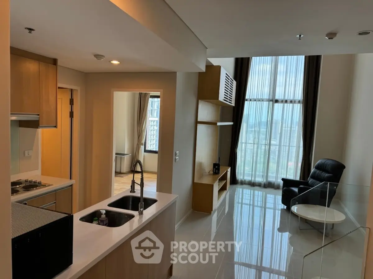 Modern open-plan living room with kitchen and floor-to-ceiling windows offering city views.