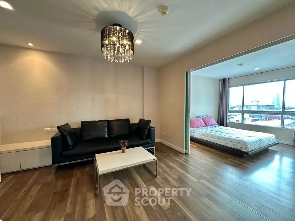 Spacious open-plan living room with elegant chandelier and cozy bedroom view.