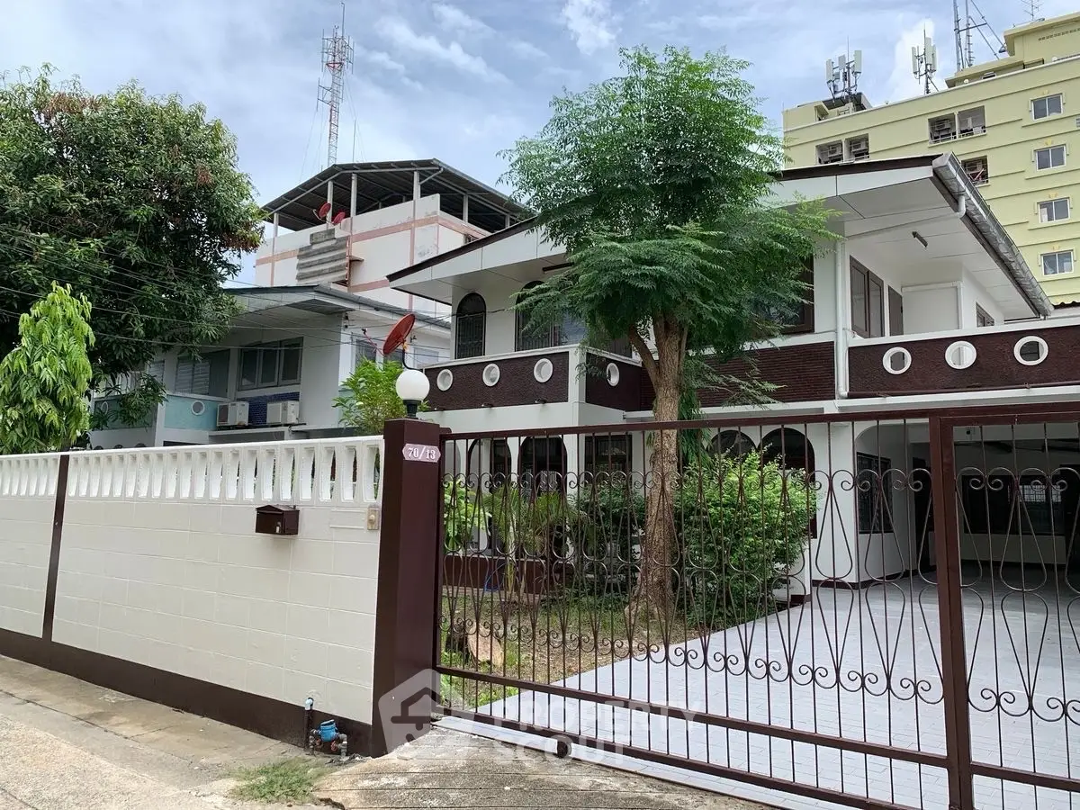 Charming two-story house with gated driveway and lush greenery in a serene neighborhood.