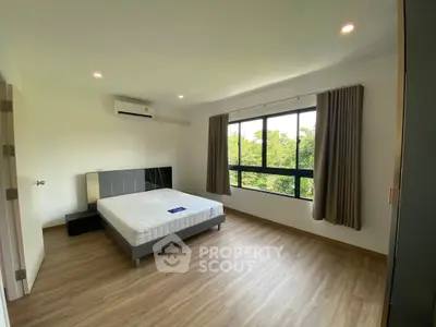 Spacious bedroom with large window and modern furnishings, offering a serene view of greenery.