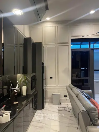 Modern living room with sleek design, featuring a gray sofa, elegant paneling, and a stylish kitchen area.