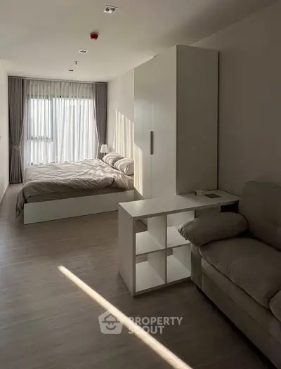 Modern bedroom with cozy bed, stylish sofa, and natural light through large window.