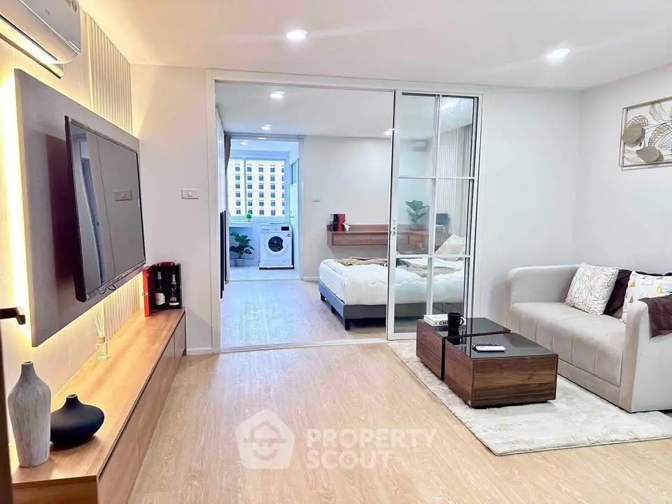 Modern living room with cozy sofa, TV, and view into stylish bedroom with washing machine.