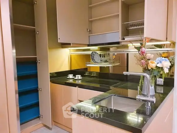 Modern kitchen with sleek cabinets and black countertops, featuring a stylish sink and floral arrangement.