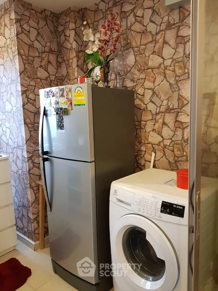 Cozy kitchen corner with fridge and washing machine, stone-patterned wall adds rustic charm.