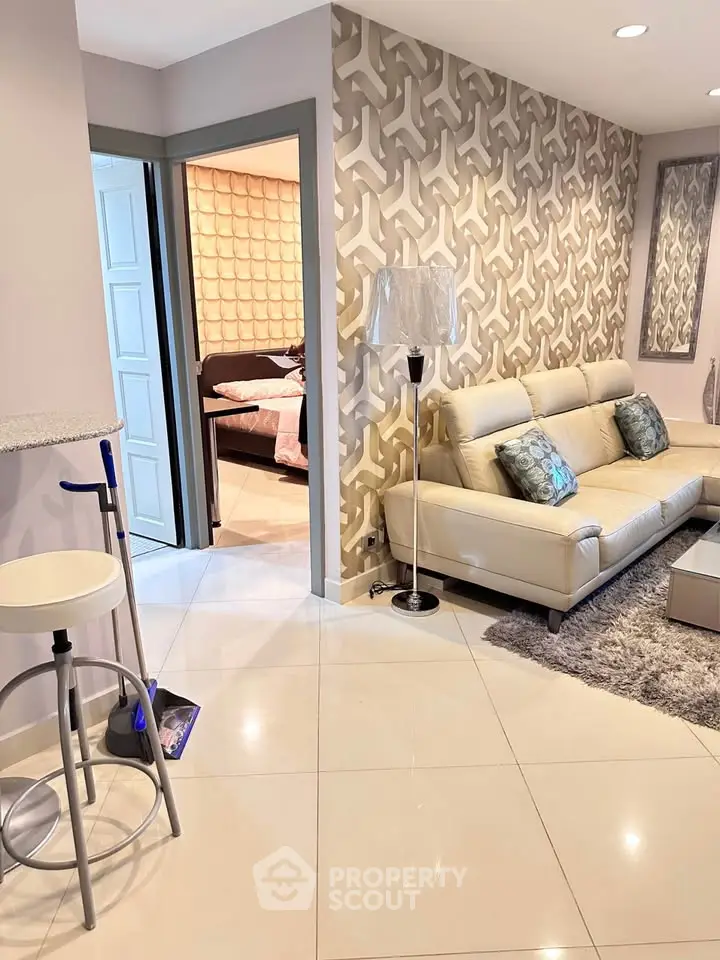 Modern living room with stylish decor and open view into a cozy bedroom, featuring elegant furniture and unique wall patterns.