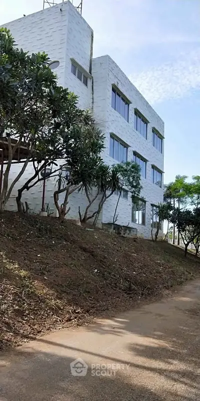 Modern three-story building with large windows and lush greenery, ideal for commercial or residential use.