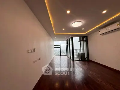 Spacious modern living room with wooden flooring and balcony view in high-rise apartment.
