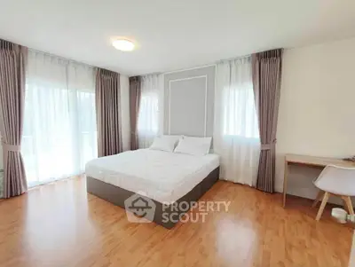 Spacious bedroom with large windows and elegant curtains, featuring a comfortable bed and a stylish desk.