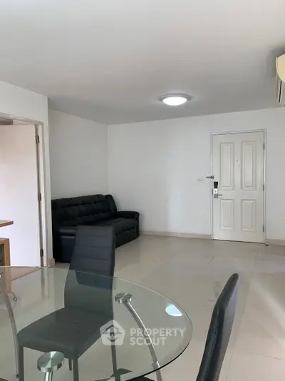 Modern living room with sleek glass dining table and black leather sofa, featuring minimalist design and bright lighting.