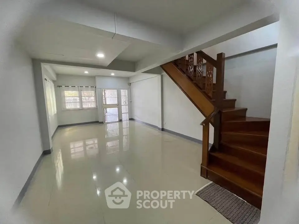 Spacious open-plan living area with glossy tiled floors and wooden staircase in modern home.
