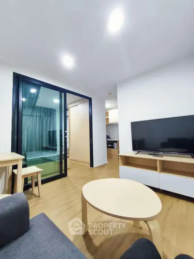 Modern living room with sleek furniture and large TV, open layout to kitchen area