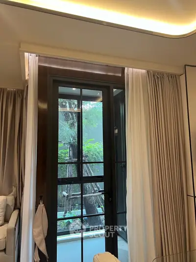 Elegant living room with large window doors opening to a lush garden view, featuring modern curtains and cozy seating.
