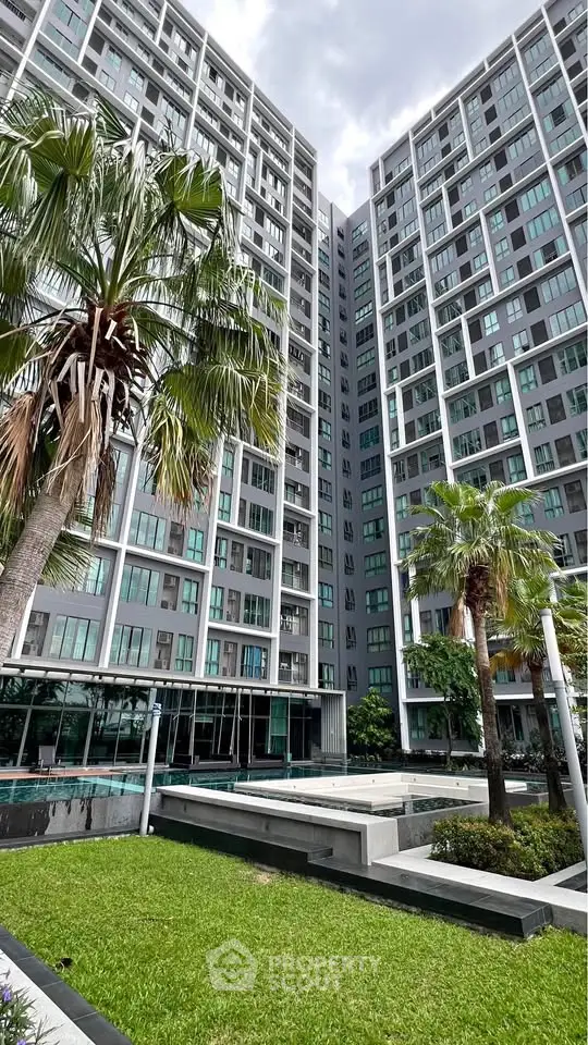 Modern high-rise residential building with lush green landscaping and palm trees.