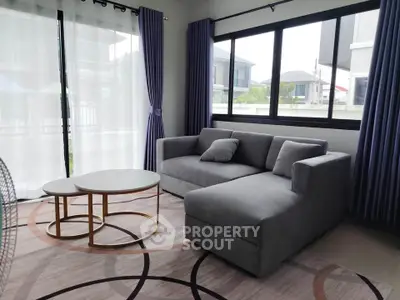 Modern living room with stylish gray sofa and elegant round coffee tables, featuring large windows and chic curtains.