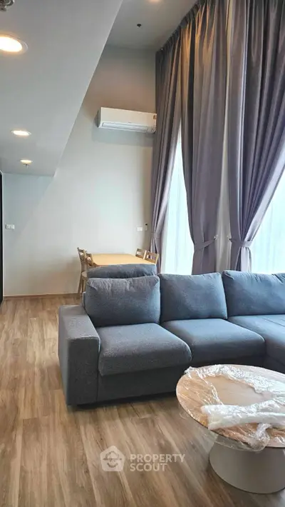 Modern living room with stylish gray sofa, wooden flooring, and elegant curtains in a contemporary apartment.