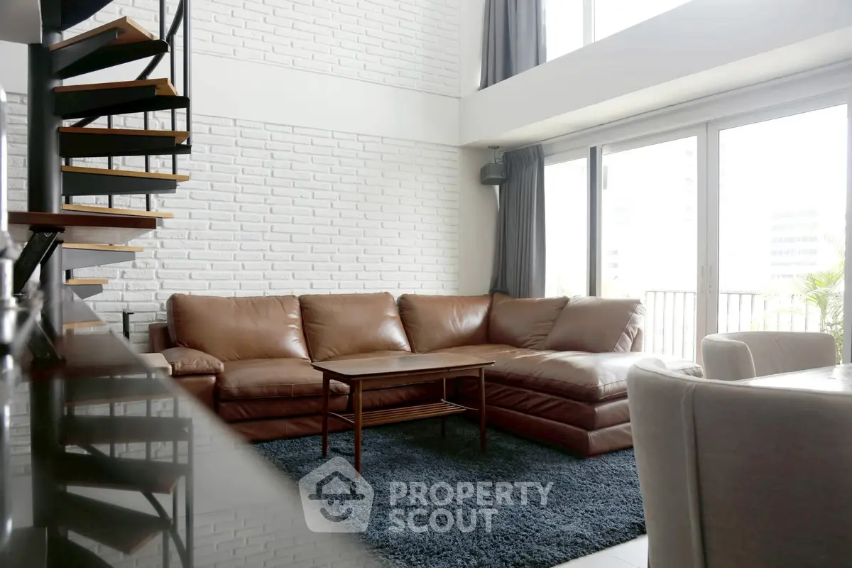 Modern living room with leather sofa and spiral staircase, featuring large windows and a cozy atmosphere.