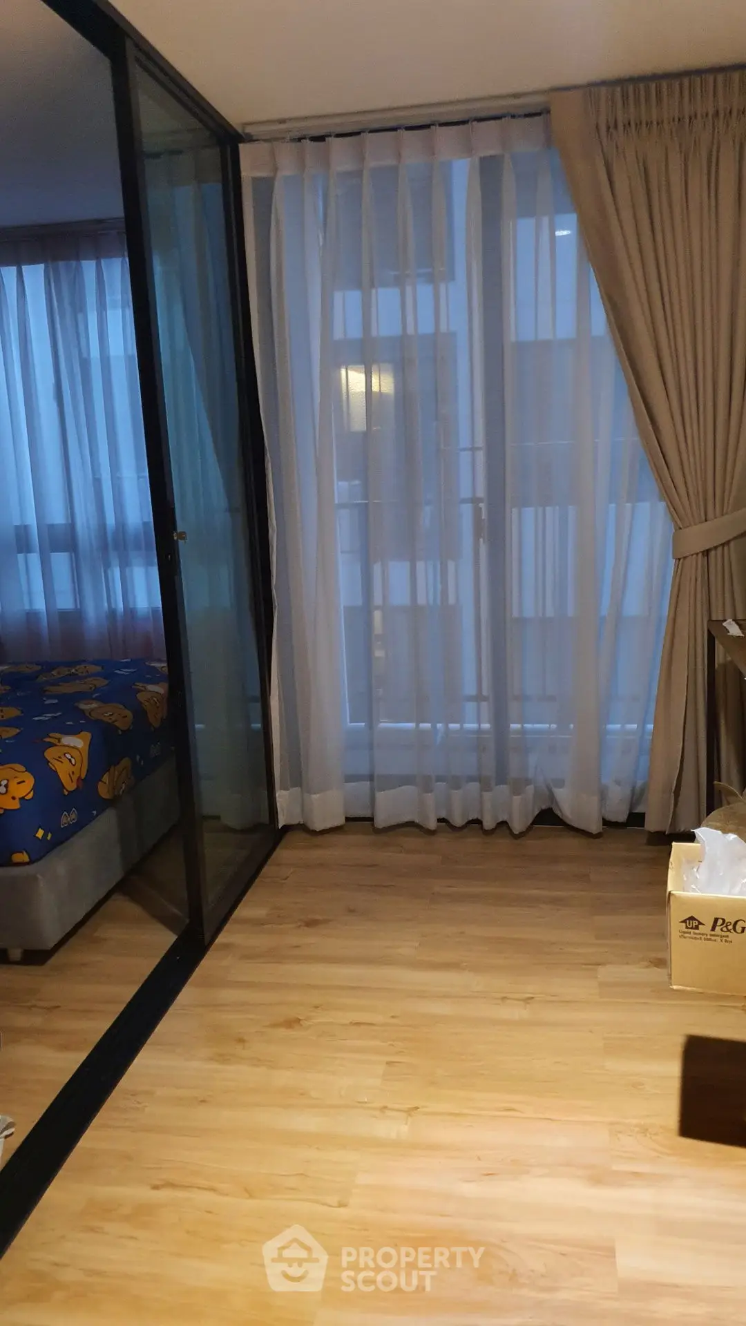 Cozy bedroom with wooden flooring and large windows with curtains, perfect for natural light.