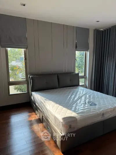 Spacious bedroom with large windows and modern decor, featuring a comfortable bed and elegant curtains.