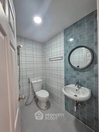 Modern bathroom with sleek tiles and round mirror, featuring a toilet and sink.