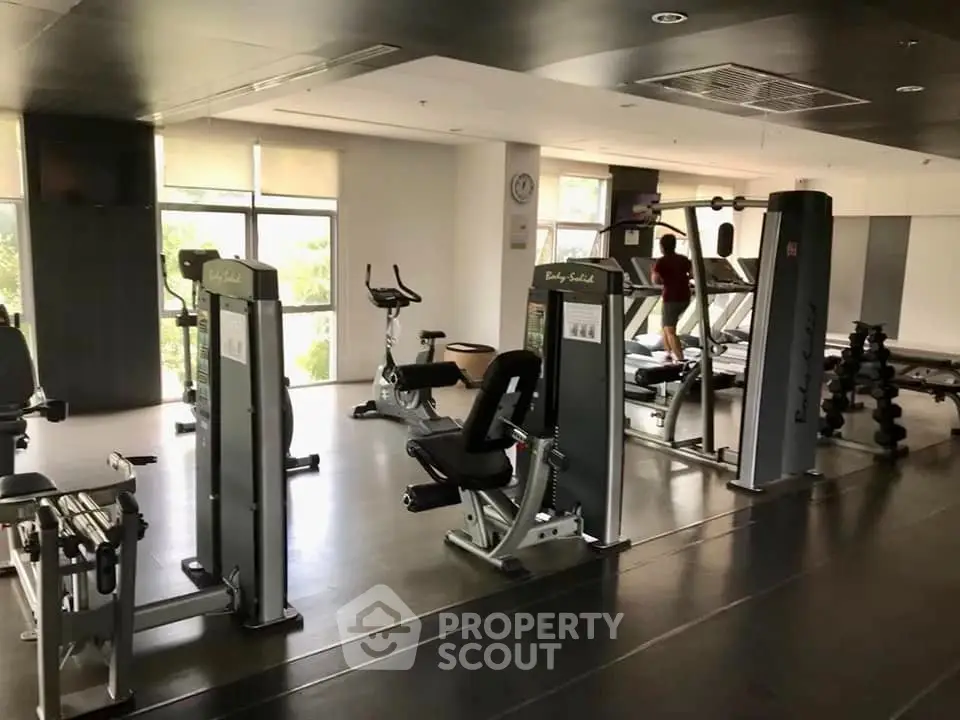 Spacious gym with modern fitness equipment and large windows for natural light.