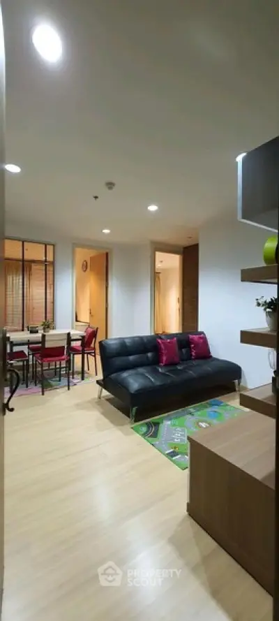 Modern living room with sleek black sofa and dining area in open layout apartment.