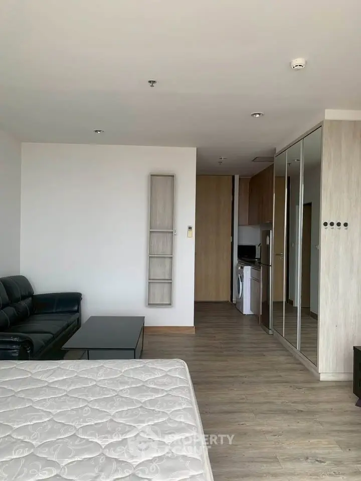 Modern studio apartment with sleek furnishings and mirrored closet doors, featuring a compact kitchen area.