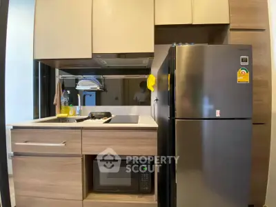 Modern kitchen with sleek cabinetry, stainless steel fridge, and built-in microwave in compact layout.