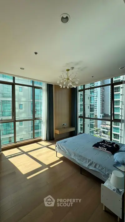 Spacious bedroom with large windows and modern decor in urban apartment.