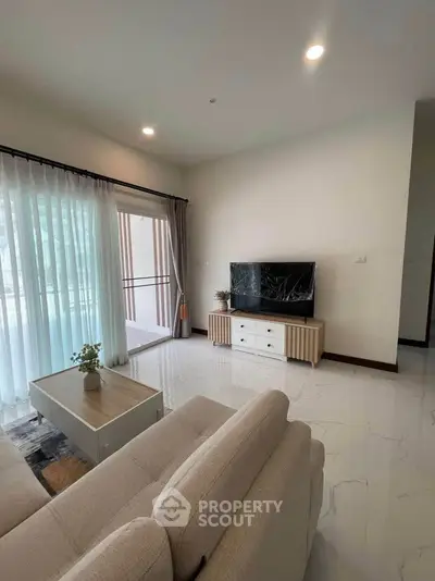Modern living room with elegant decor and natural light, featuring a cozy sofa and sleek TV setup.