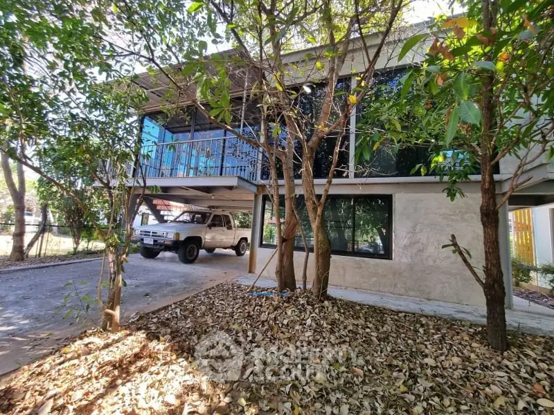 Charming two-story home with carport surrounded by lush trees and natural landscaping.
