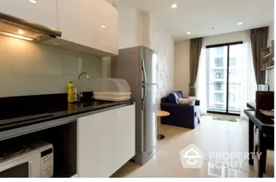 Modern kitchen with sleek white cabinetry and stainless steel appliances opens to a cozy living area with natural light streaming from the balcony.