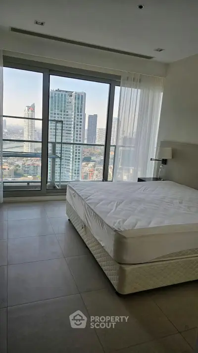 Spacious bedroom with large windows offering stunning city views in a modern high-rise apartment.