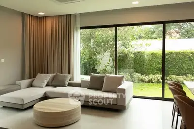 Spacious living room with large windows overlooking a lush garden, featuring modern furniture and elegant decor.