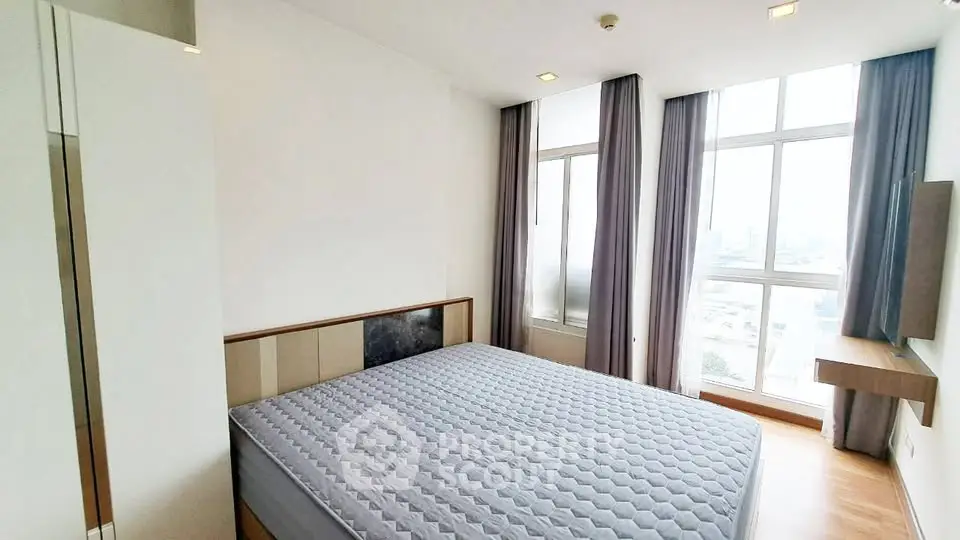 Spacious bedroom with large windows and modern decor in a high-rise apartment.