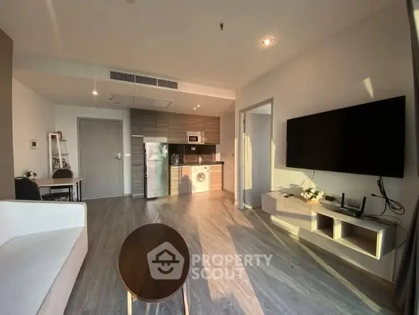 Modern living room with open kitchen, sleek furniture, and natural light.