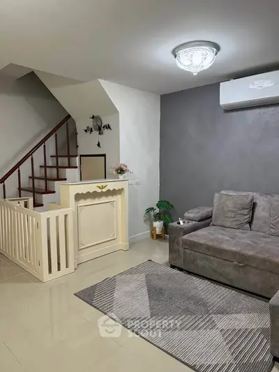 Modern living room with stylish gray sofa and elegant staircase, featuring chic decor and air conditioning.