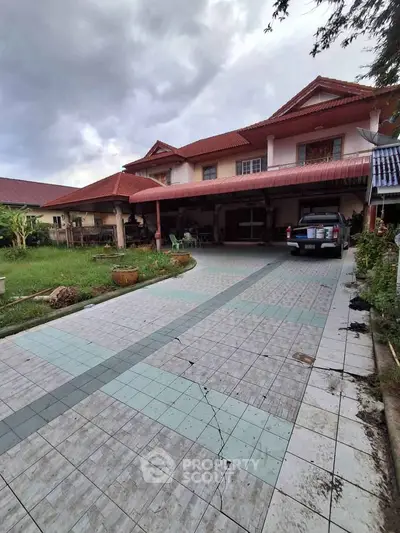 Spacious two-story house with tiled driveway and carport, featuring a lush garden and traditional architecture.