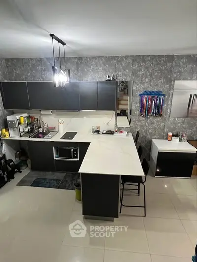 Modern kitchen with sleek black cabinets and white countertops, featuring a built-in microwave and stylish lighting.
