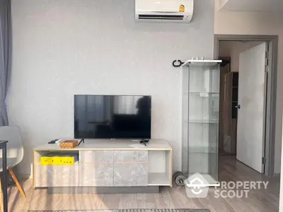 Modern minimalist living room with sleek TV stand, large flat-screen TV, and elegant glass display cabinet, complemented by soft gray tones and wood flooring.