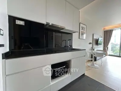 Modern open-layout kitchen with sleek black countertops and integrated appliances, leading to a bright living area with a view.