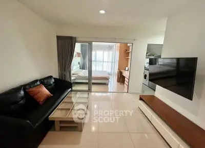 Modern living room with sleek black sofa, glass coffee table, and wall-mounted TV, leading to a cozy bedroom.