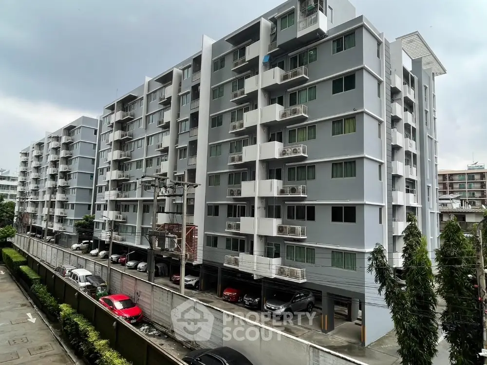 Modern multi-story residential building with balconies and parking area in urban setting.