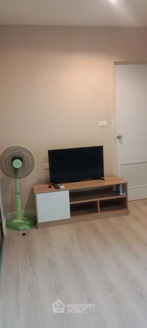 Modern living room with TV stand and fan, featuring light wood flooring and neutral wall tones.