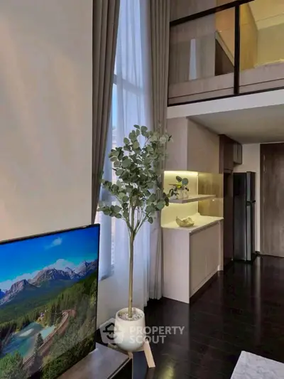 Modern living room with high ceilings and mezzanine, featuring sleek kitchen and large window.