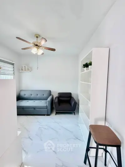 Modern living room with sleek furniture and ceiling fan, featuring a cozy sofa and armchair.