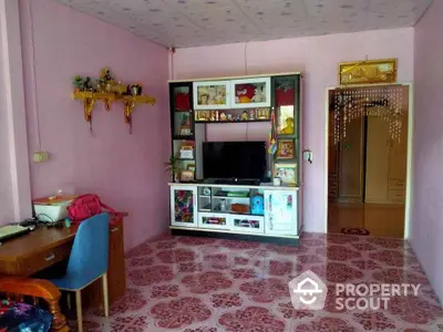 Charming living room with pink walls and decorative shelving, featuring a cozy TV setup and patterned flooring.