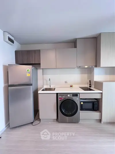 Modern kitchen with sleek cabinets, stainless steel fridge, washing machine, and microwave in a compact layout.