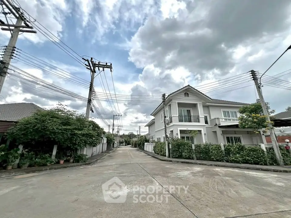 Charming suburban house with lush greenery and spacious driveway under cloudy sky.